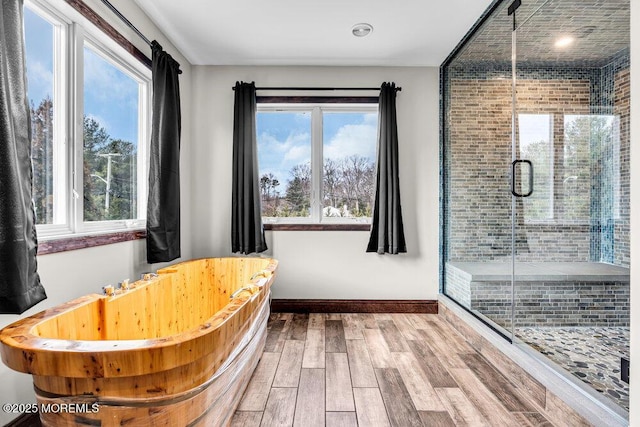 bathroom featuring a stall shower, a freestanding tub, baseboards, and wood finished floors