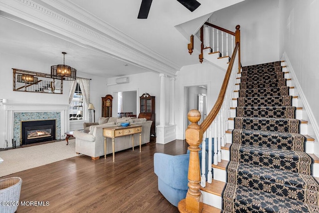 stairs with crown molding, decorative columns, a fireplace with flush hearth, an AC wall unit, and wood finished floors