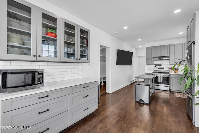 kitchen featuring under cabinet range hood, a baseboard radiator, gray cabinets, and stainless steel appliances