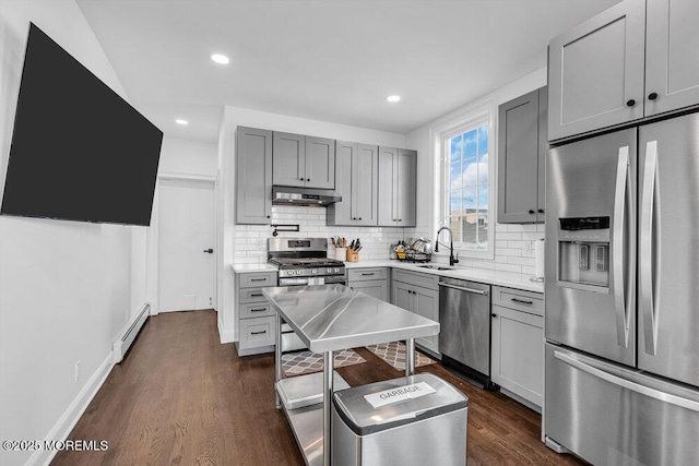 kitchen featuring stainless steel appliances, baseboard heating, gray cabinetry, a sink, and under cabinet range hood