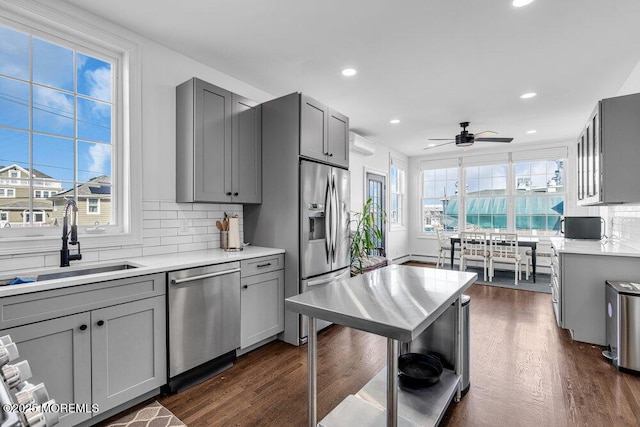 kitchen featuring dark wood-style flooring, a wall unit AC, stainless steel appliances, gray cabinetry, and a sink