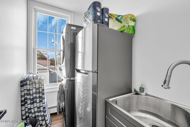 washroom with stacked washer and dryer, a baseboard radiator, a healthy amount of sunlight, a sink, and laundry area