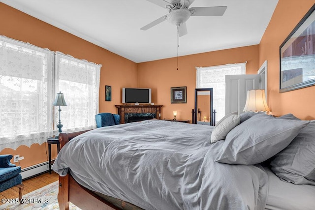 bedroom featuring a baseboard heating unit, ceiling fan, and wood finished floors