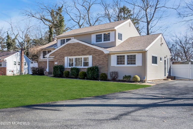 traditional home featuring a front lawn, fence, brick siding, and roof with shingles