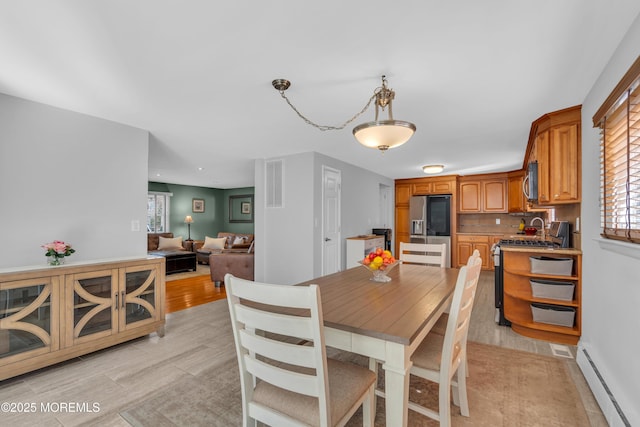 dining room with visible vents, light wood-type flooring, and a baseboard heating unit