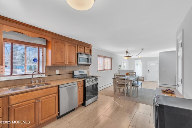 kitchen with backsplash, baseboard heating, brown cabinets, stainless steel appliances, and a sink