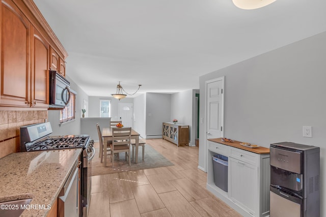 kitchen with stainless steel gas stove, light stone counters, backsplash, baseboards, and baseboard heating