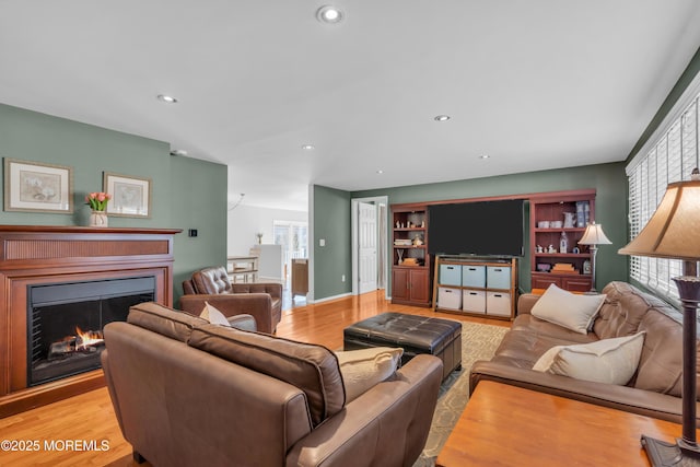 living room featuring recessed lighting, wood finished floors, baseboards, and a lit fireplace