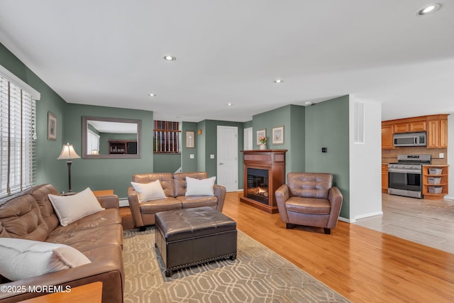 living room featuring baseboards, recessed lighting, light wood-style floors, a glass covered fireplace, and a baseboard heating unit