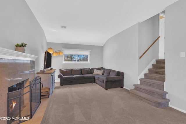 living area with visible vents, a tiled fireplace, stairway, vaulted ceiling, and carpet flooring