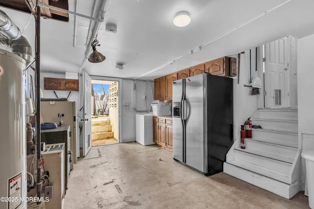 kitchen with concrete flooring, light countertops, stainless steel refrigerator with ice dispenser, brown cabinetry, and washer / clothes dryer