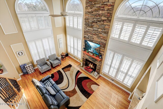 living room featuring visible vents, a ceiling fan, a towering ceiling, wood finished floors, and a stone fireplace