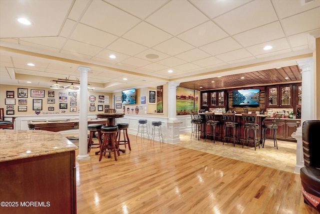 interior space featuring a community bar, a decorative wall, light wood finished floors, and ornate columns