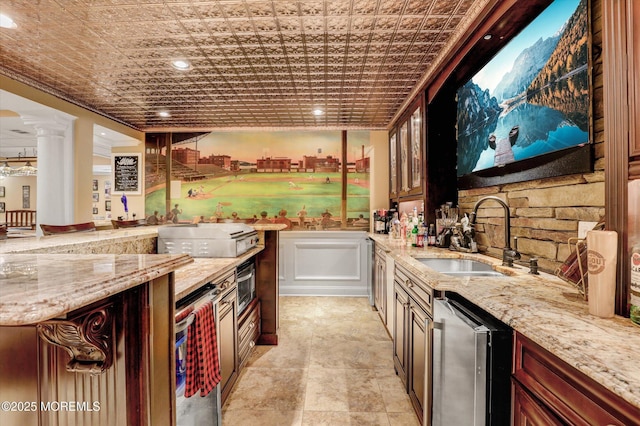 kitchen with decorative columns, light stone counters, a sink, and an ornate ceiling