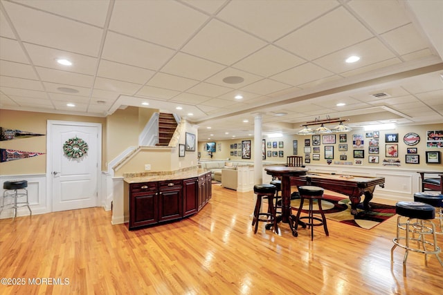 bar featuring a wainscoted wall, visible vents, light wood-style flooring, and stairs