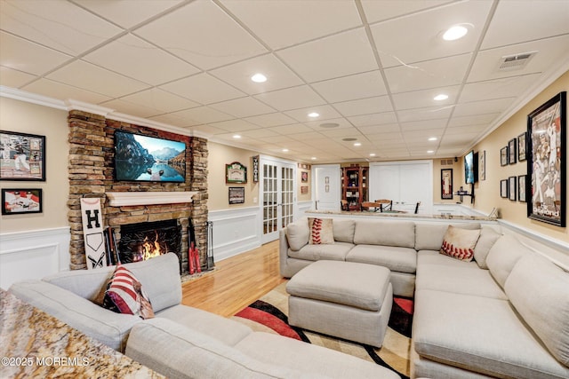 living area with light wood-style flooring, visible vents, crown molding, and a stone fireplace