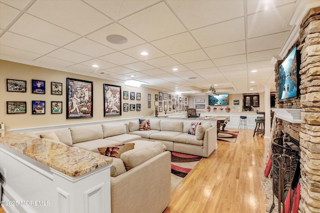 living room with light wood-type flooring, a fireplace, a paneled ceiling, and recessed lighting