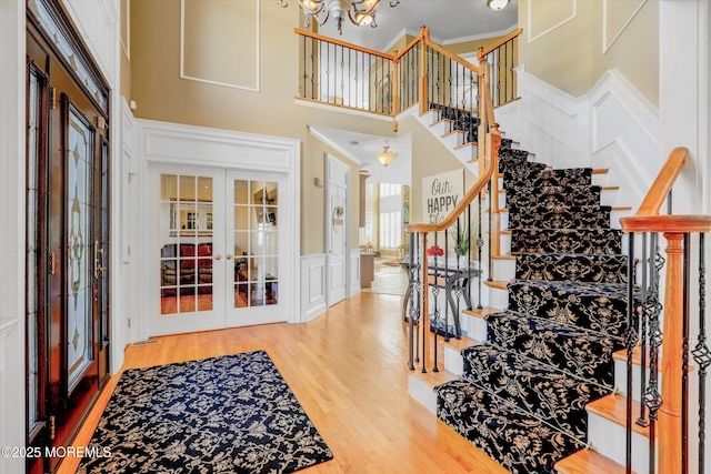 entryway with a decorative wall, a high ceiling, wood finished floors, french doors, and an inviting chandelier