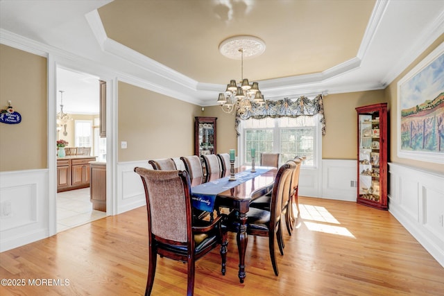 dining room with a chandelier, a tray ceiling, a healthy amount of sunlight, and light wood-style flooring