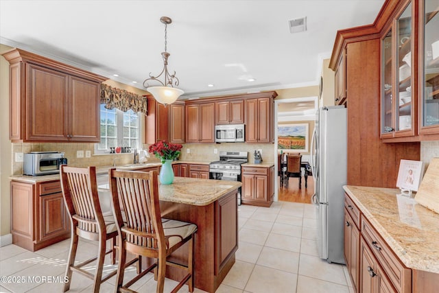 kitchen featuring stainless steel appliances, brown cabinetry, visible vents, and a breakfast bar area