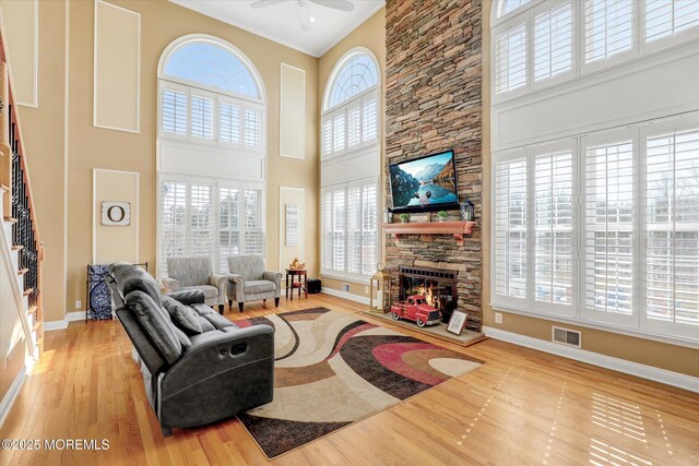 living area featuring a stone fireplace, wood finished floors, a ceiling fan, visible vents, and baseboards