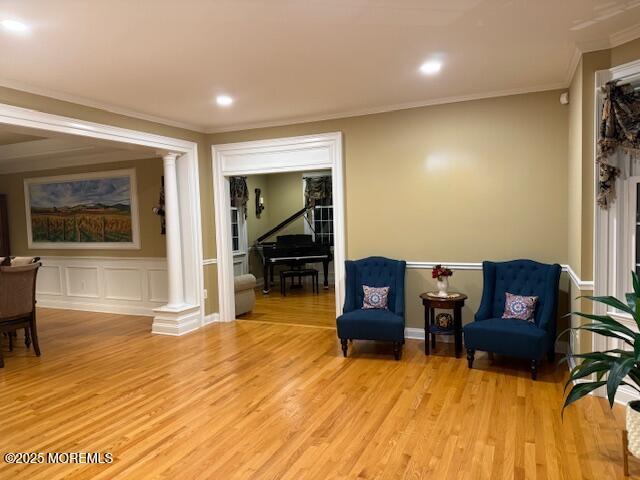 sitting room featuring light wood-style flooring, decorative columns, and crown molding