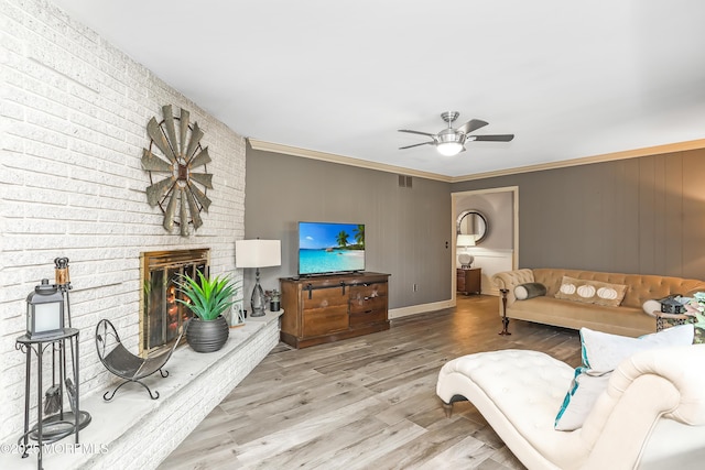 living area with a ceiling fan, wood finished floors, visible vents, crown molding, and a brick fireplace