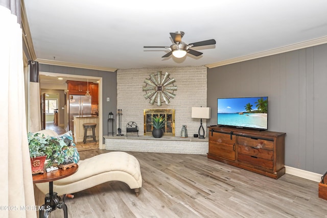 living room featuring crown molding, baseboards, ceiling fan, light wood-type flooring, and a fireplace