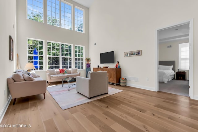 living area featuring visible vents, light wood finished floors, a high ceiling, and baseboards