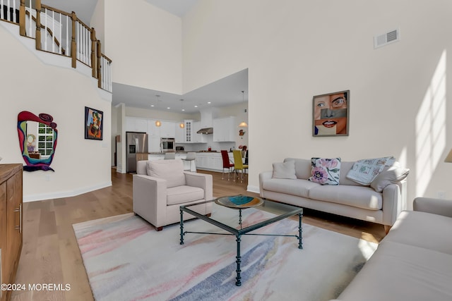 living room with a high ceiling, light wood-type flooring, visible vents, and baseboards