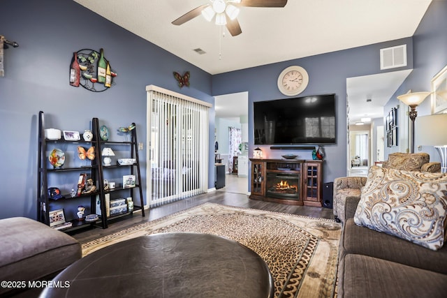 living room featuring visible vents, a ceiling fan, wood finished floors, a lit fireplace, and baseboards