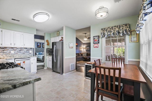 kitchen featuring tasteful backsplash, white cabinets, stainless steel fridge, and visible vents