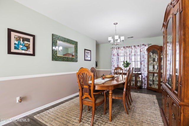 dining space featuring baseboards, visible vents, a notable chandelier, and wood finished floors