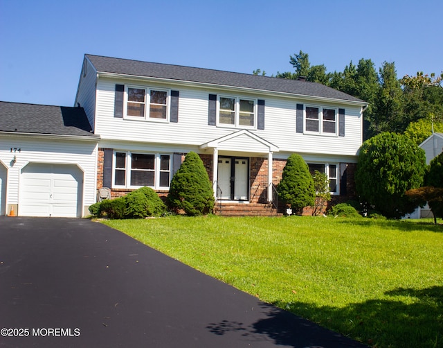 colonial-style house featuring aphalt driveway, a front yard, brick siding, and an attached garage