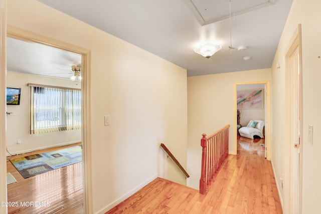 hall featuring an upstairs landing, light wood-style flooring, attic access, and baseboards