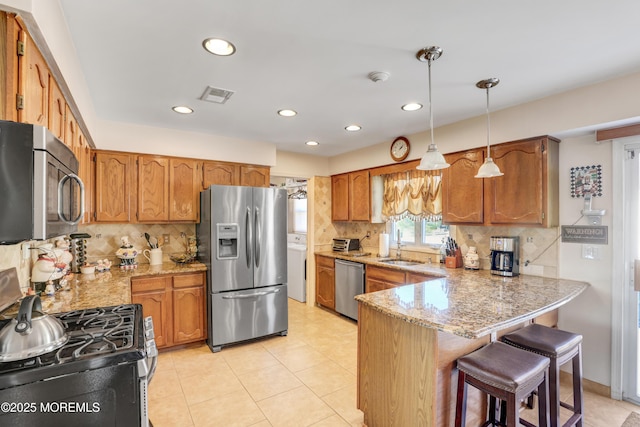 kitchen featuring a breakfast bar area, visible vents, a peninsula, stainless steel appliances, and brown cabinets