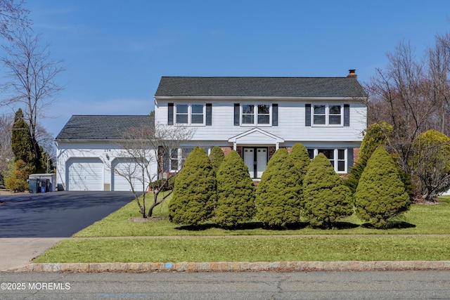 view of front of home featuring aphalt driveway, a front lawn, a chimney, and an attached garage