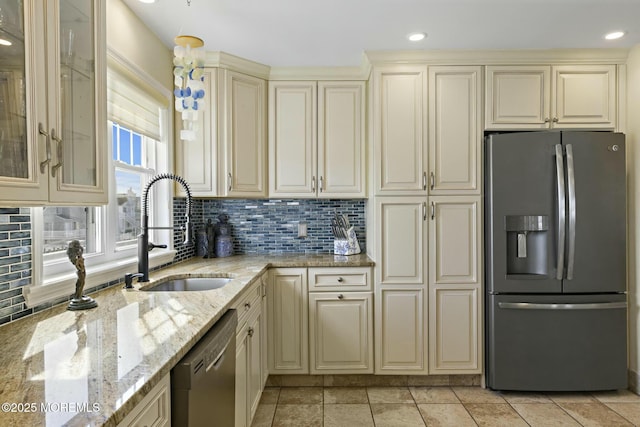 kitchen with decorative backsplash, light stone counters, appliances with stainless steel finishes, cream cabinetry, and a sink