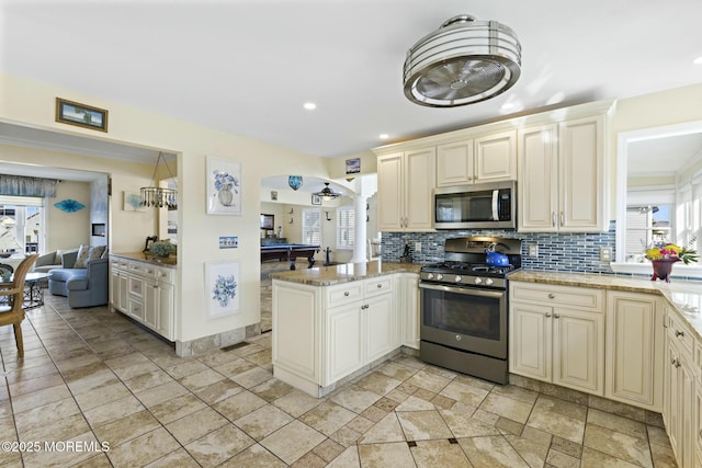 kitchen with appliances with stainless steel finishes, a healthy amount of sunlight, backsplash, and cream cabinets