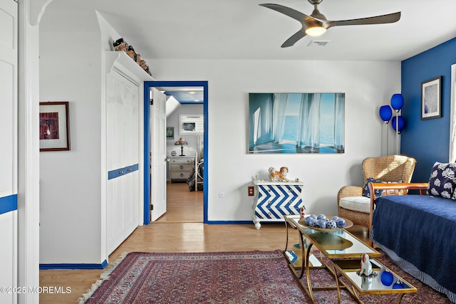 living area featuring baseboards, wood finished floors, visible vents, and a ceiling fan