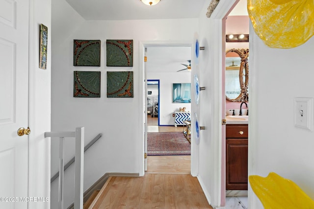 hallway with light wood-type flooring, a sink, an upstairs landing, and baseboards