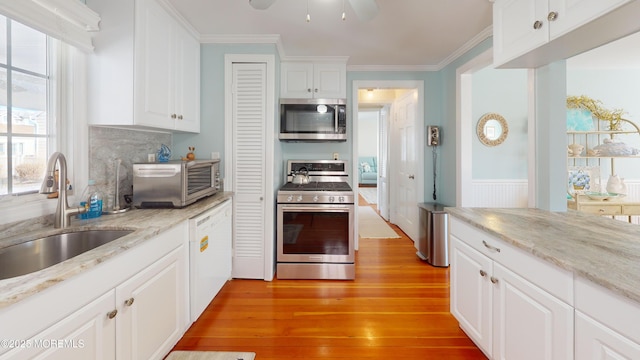 kitchen featuring a toaster, stainless steel appliances, light wood-style flooring, ornamental molding, and a sink