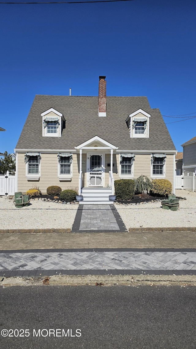 cape cod home featuring covered porch, a shingled roof, a chimney, and fence