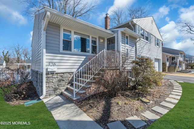 view of front of property featuring stone siding, fence, a chimney, and an attached garage