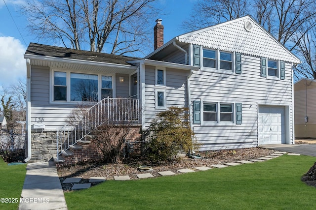 split level home with an attached garage, aphalt driveway, a chimney, and a front lawn