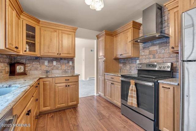 kitchen featuring light stone counters, appliances with stainless steel finishes, glass insert cabinets, light wood-style floors, and wall chimney range hood