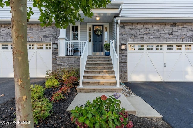 view of exterior entry with a garage, stone siding, a porch, and driveway