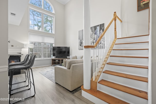 living room featuring a wealth of natural light, visible vents, a glass covered fireplace, and a towering ceiling