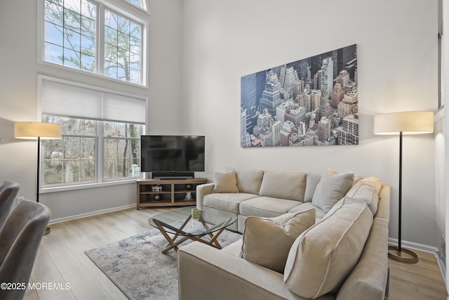 living room with baseboards, a healthy amount of sunlight, a high ceiling, and wood finished floors