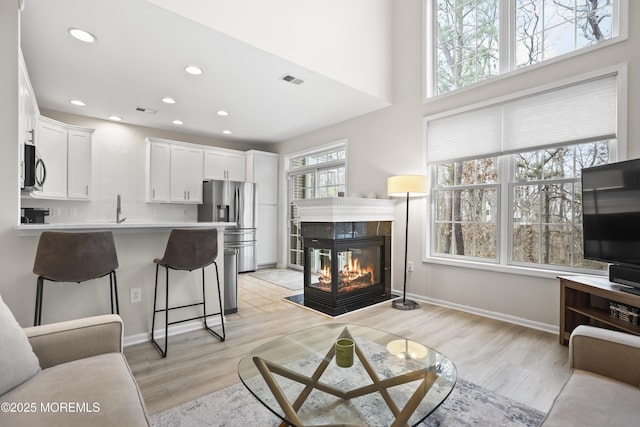 living room with light wood-type flooring, visible vents, a tiled fireplace, and recessed lighting